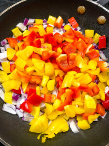 A frying pan with diced red onion, red bell pepper, and yellow bell pepper. Cooking With Fudge