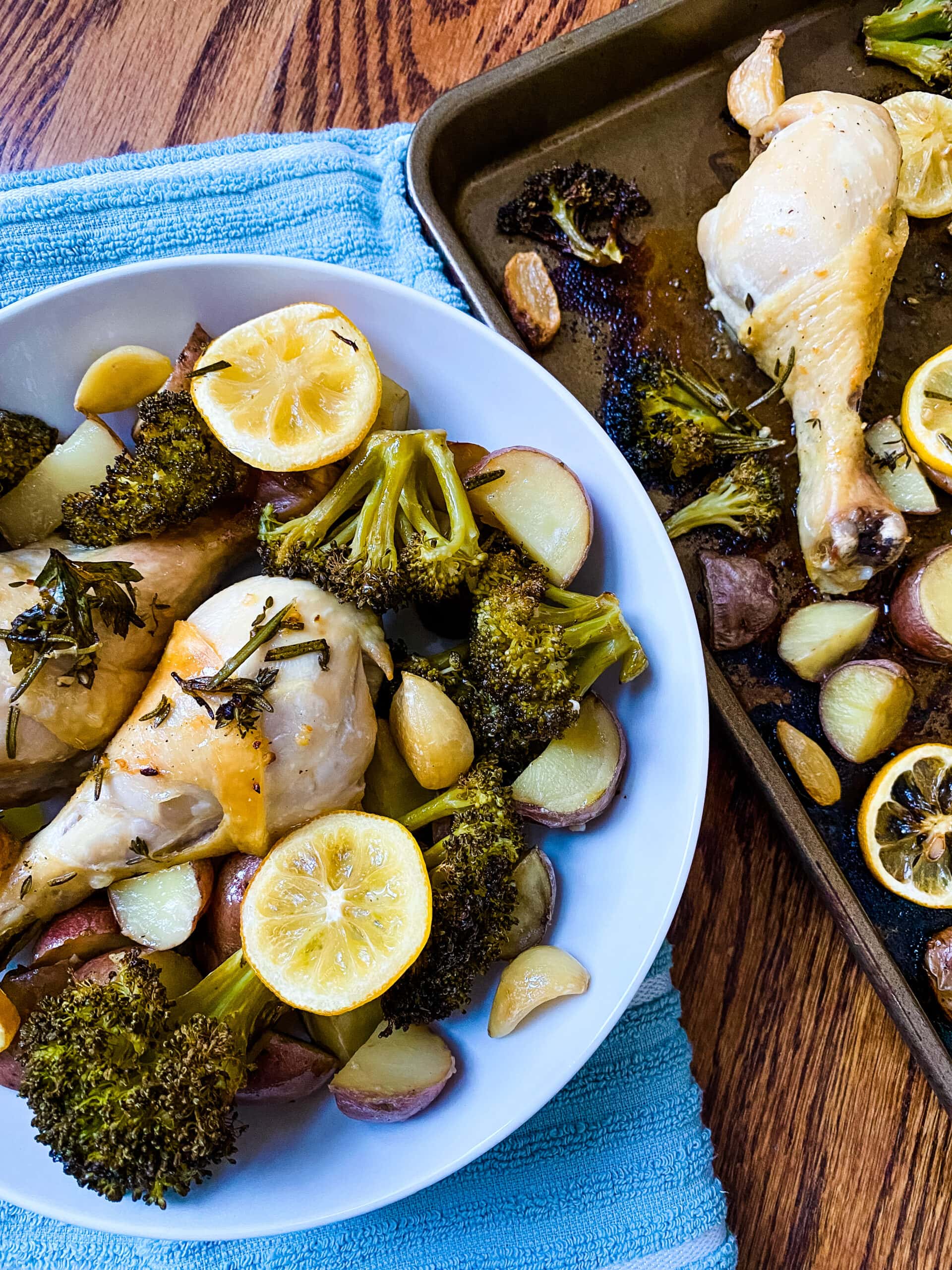 A bowl and sheet pan with chicken drumsticks, broccoli florets, baby red potatoes, lemon slices, and garlic cloves for Sheet Pan Lemon Garlic Chicken. Cooking With Fudge
