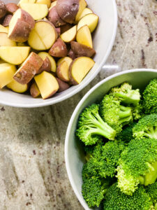 One bowl with cut baby red potatoes and one bowl with broccoli florets. Cooking With Fudge