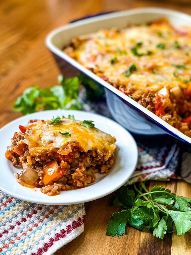 A plate with a serving of Stuffed Pepper Bake and a baking dish in the background. Cooking With Fudge